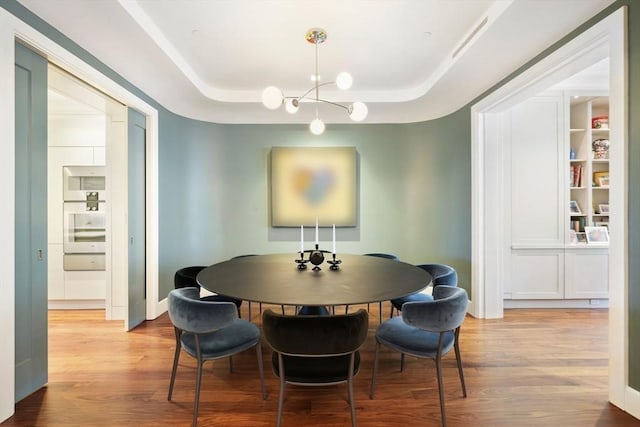 dining space featuring light wood finished floors, built in features, an inviting chandelier, and a tray ceiling