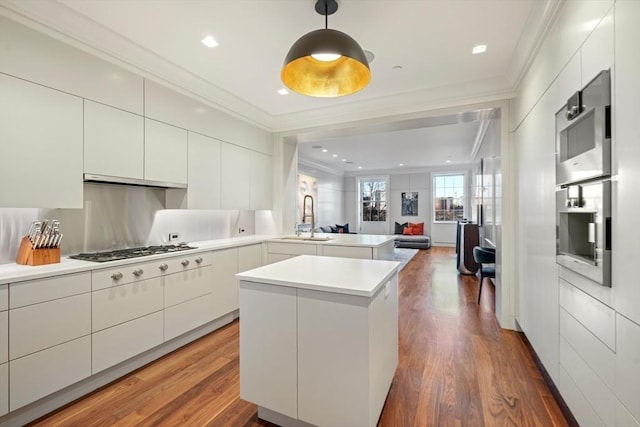 kitchen featuring modern cabinets, a sink, open floor plan, crown molding, and light countertops