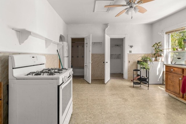 kitchen featuring brown cabinets, ceiling fan, wainscoting, light floors, and white range with gas cooktop