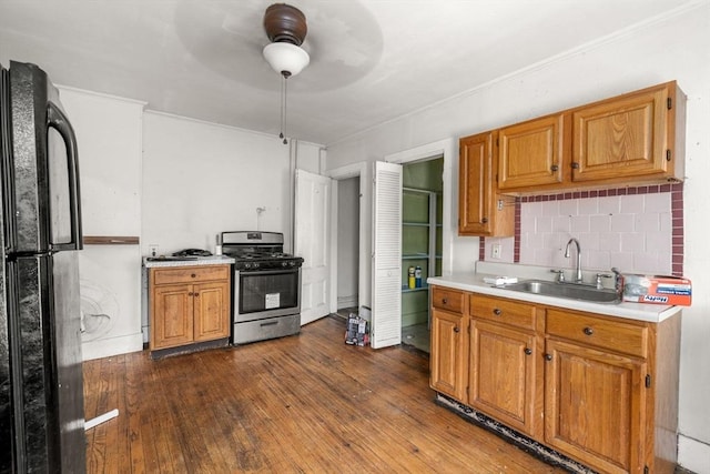 kitchen with freestanding refrigerator, stainless steel gas stove, dark wood-type flooring, light countertops, and a sink