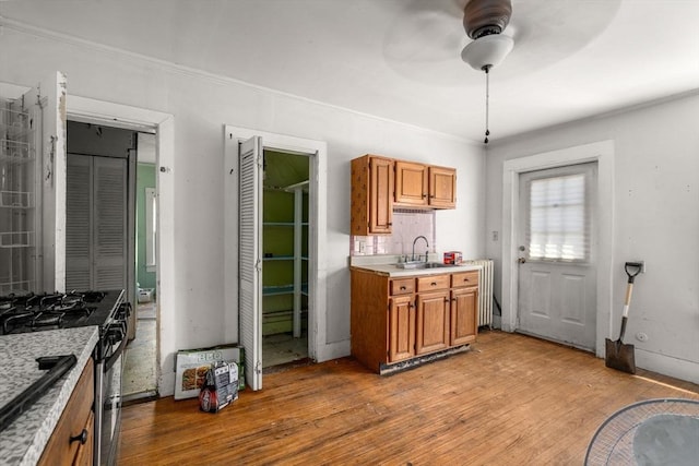 kitchen with brown cabinets, a ceiling fan, light wood-style floors, and gas range