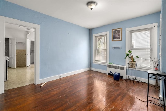 spare room featuring baseboards, wood finished floors, and radiator
