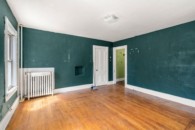 spare room featuring radiator heating unit, baseboards, and wood-type flooring