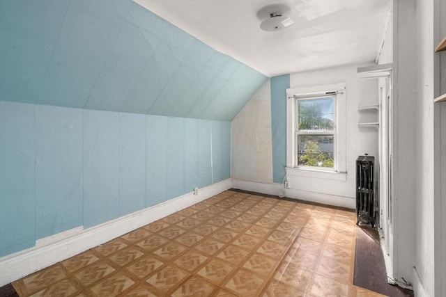 additional living space with baseboards, light floors, and vaulted ceiling