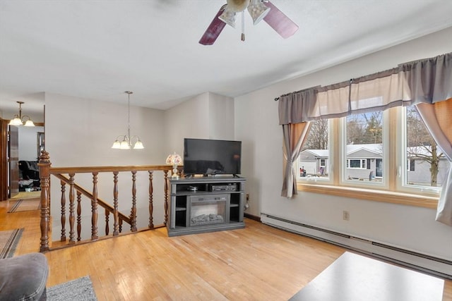 living room with a baseboard heating unit, ceiling fan with notable chandelier, and wood-type flooring