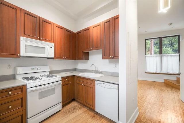 kitchen featuring a sink, light wood finished floors, white appliances, and light countertops
