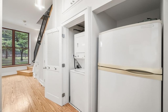 clothes washing area featuring laundry area, stacked washer and clothes dryer, and light wood-style floors