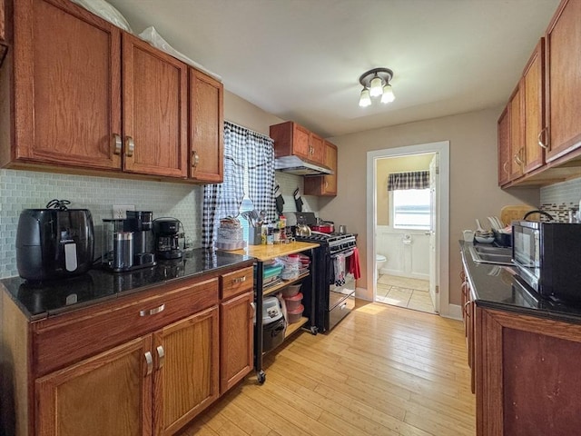 kitchen with brown cabinets, backsplash, black gas range, and under cabinet range hood