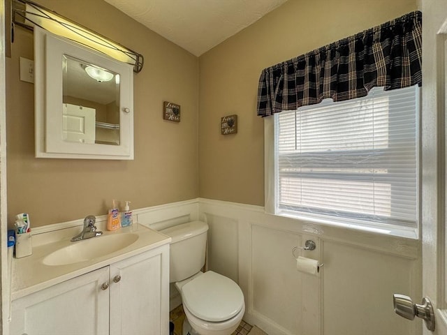 half bathroom with toilet, a wainscoted wall, a decorative wall, and vanity