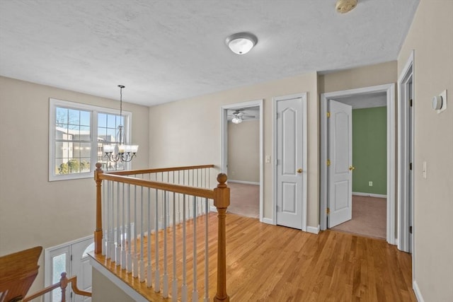 corridor featuring light wood-style flooring, an upstairs landing, a chandelier, a textured ceiling, and baseboards