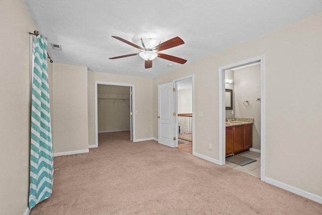 unfurnished bedroom featuring light carpet, a walk in closet, a sink, baseboards, and a closet