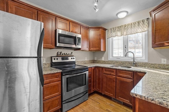 kitchen featuring appliances with stainless steel finishes, a sink, light wood finished floors, and light stone counters