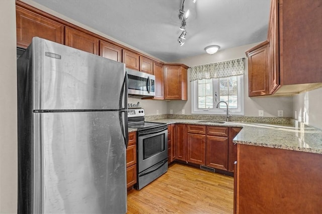 kitchen featuring stainless steel appliances, a sink, light stone countertops, light wood-type flooring, and brown cabinetry