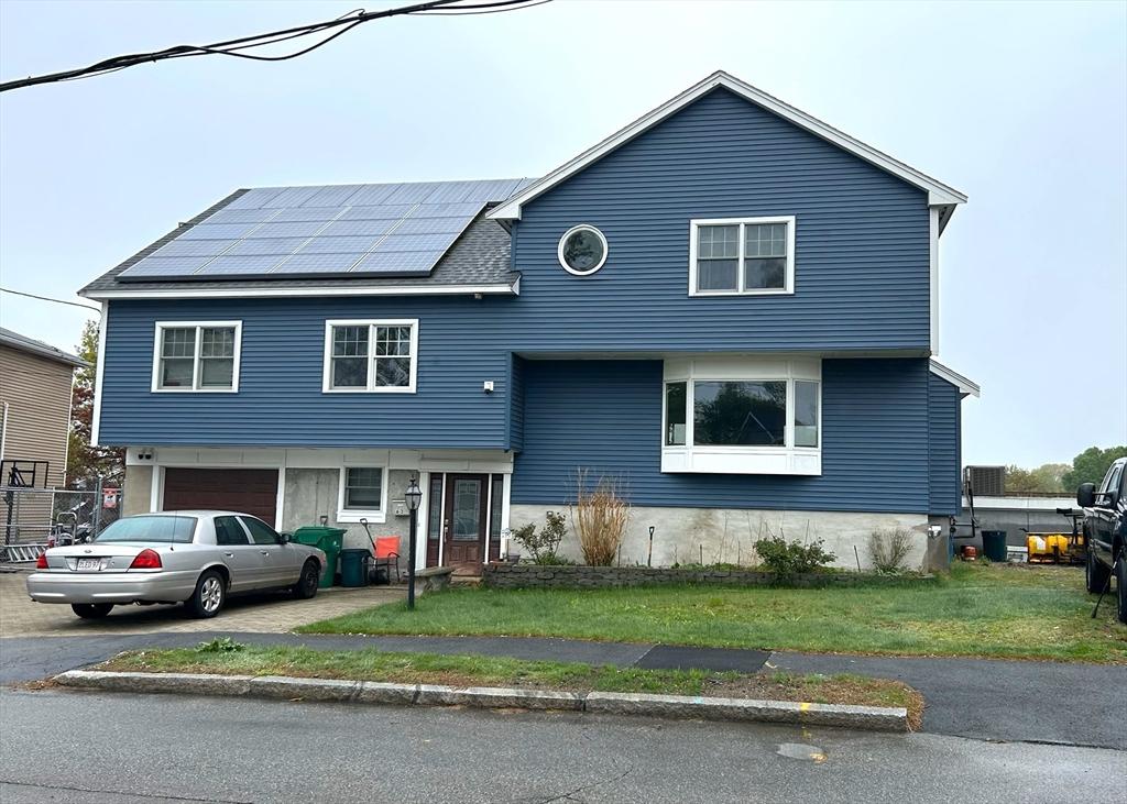 63 Doonan St, Medford, MA 02155 - view of front of house with solar panels, asphalt driveway, an attached garage, and a front lawn