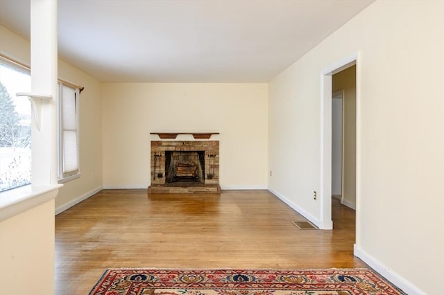 unfurnished living room featuring baseboards, a fireplace with raised hearth, visible vents, and light wood finished floors