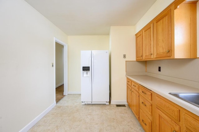 kitchen featuring white refrigerator with ice dispenser, baseboards, light countertops, and a sink