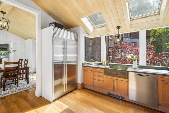 kitchen with vaulted ceiling with skylight, light hardwood / wood-style flooring, hanging light fixtures, and appliances with stainless steel finishes