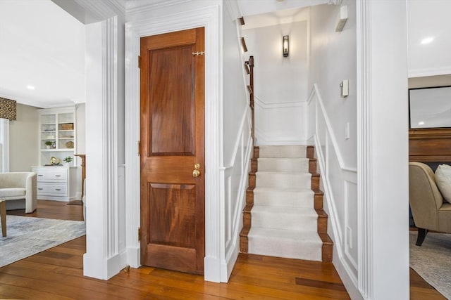 stairs with built in shelves, crown molding, and wood-type flooring