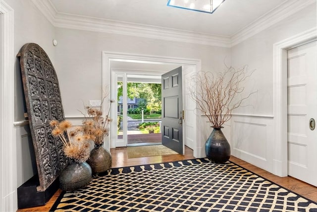 entrance foyer with a wainscoted wall, a decorative wall, wood finished floors, and crown molding