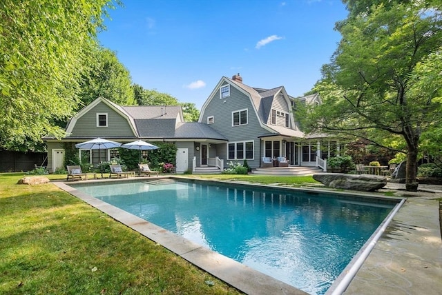 rear view of house with a lawn, a chimney, a gambrel roof, and an outdoor pool