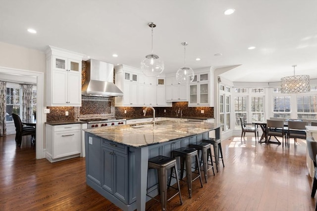 kitchen with wall chimney exhaust hood, glass insert cabinets, a large island, and decorative light fixtures