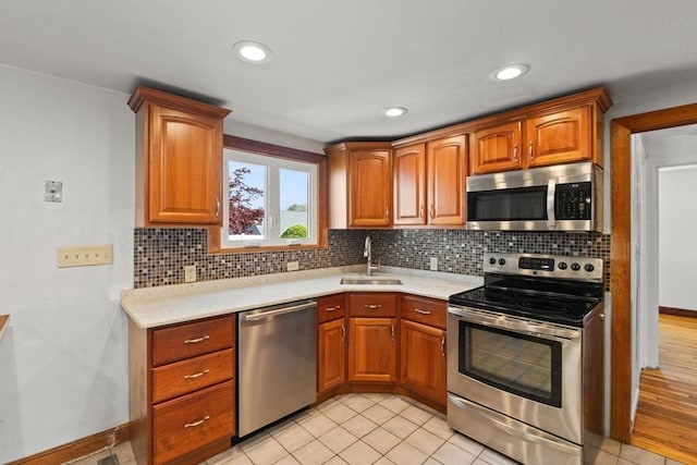 kitchen with a sink, stainless steel appliances, brown cabinets, backsplash, and light countertops