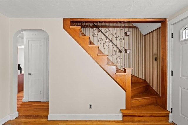 stairs with wood finished floors, baseboards, and arched walkways
