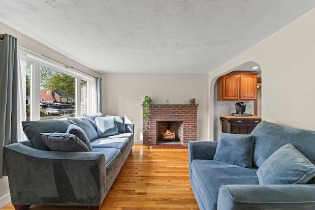 living room with light wood-style flooring, a brick fireplace, and arched walkways