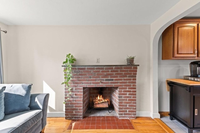 living room with a brick fireplace, baseboards, arched walkways, and light wood-style floors