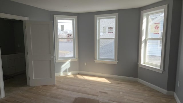 empty room featuring light wood-type flooring, a healthy amount of sunlight, and baseboards