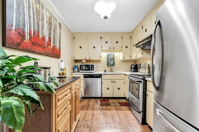 kitchen featuring sink, tasteful backsplash, stainless steel appliances, light hardwood / wood-style floors, and cream cabinetry