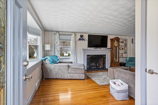 living room featuring a fireplace with raised hearth, wood finished floors, baseboards, and ornamental molding