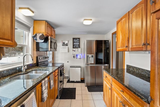 kitchen with stainless steel appliances, a sink, dark stone countertops, and light tile patterned floors