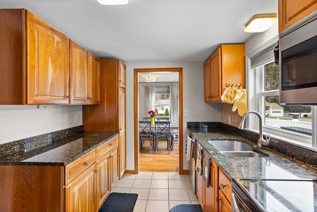 kitchen featuring a sink, appliances with stainless steel finishes, light tile patterned flooring, dark stone countertops, and brown cabinets