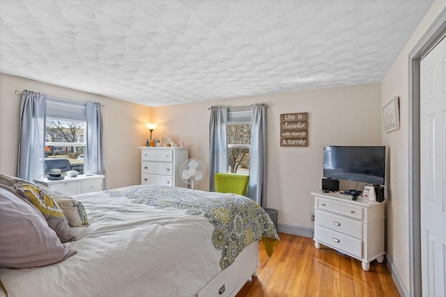 bedroom with multiple windows, light wood-style flooring, and baseboards
