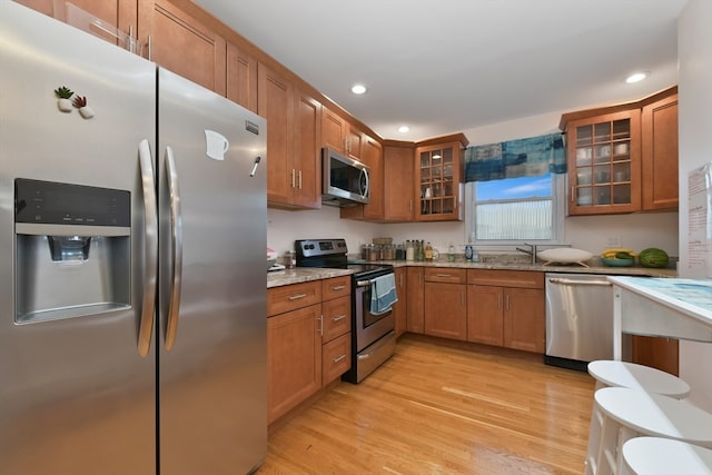 kitchen featuring sink, light stone countertops, light wood-type flooring, and stainless steel appliances