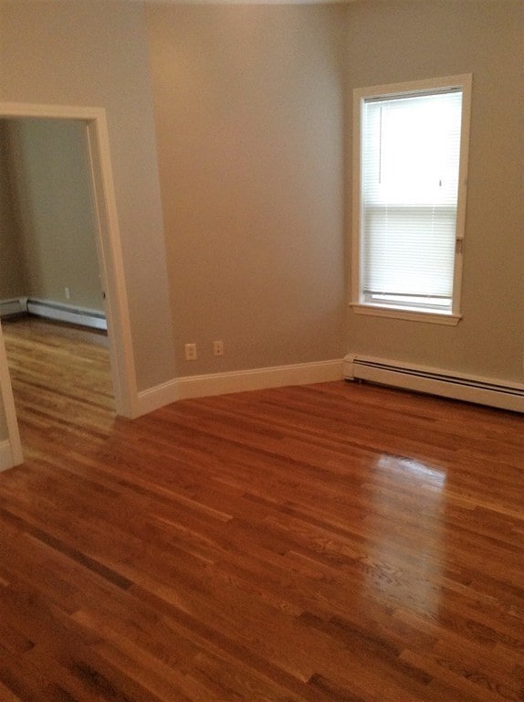 empty room with dark hardwood / wood-style floors and a baseboard radiator