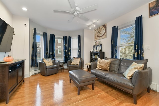 living room with ceiling fan, plenty of natural light, a baseboard heating unit, and light hardwood / wood-style flooring