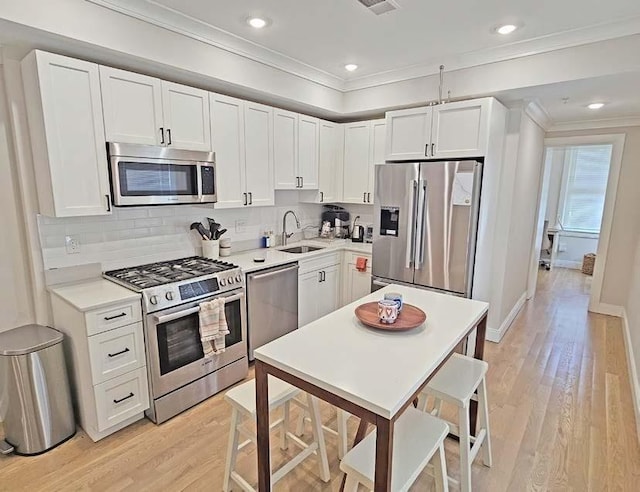 kitchen featuring stainless steel appliances, light wood-style floors, ornamental molding, and a sink