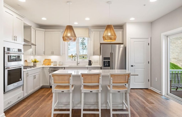 kitchen featuring sink, stainless steel appliances, a kitchen breakfast bar, a kitchen island, and decorative light fixtures