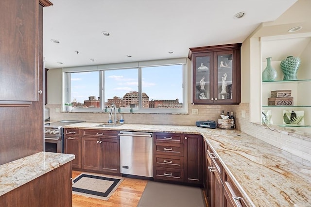 kitchen featuring appliances with stainless steel finishes, light stone counters, a sink, decorative backsplash, and glass insert cabinets