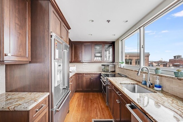 kitchen with light stone countertops, a sink, light wood-style floors, high end appliances, and tasteful backsplash