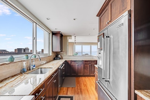 kitchen with light stone countertops, a sink, stainless steel appliances, decorative backsplash, and light wood-type flooring