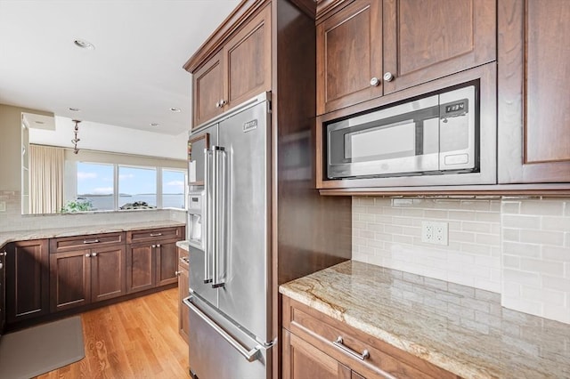 kitchen featuring light wood-type flooring, light stone counters, tasteful backsplash, and stainless steel appliances