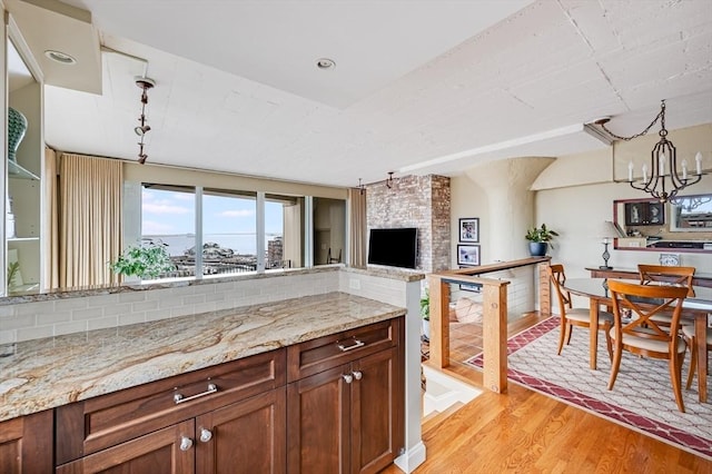 kitchen with an inviting chandelier, a stone fireplace, light wood-type flooring, light stone counters, and decorative light fixtures