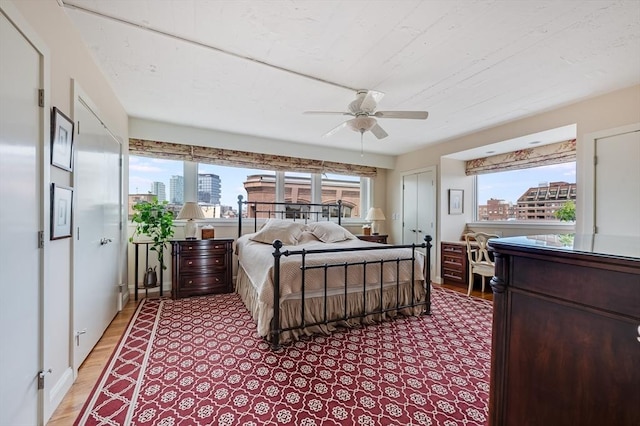 bedroom with light wood-style floors, a view of city, multiple windows, and a ceiling fan
