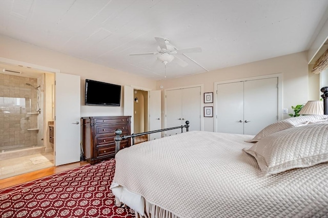 bedroom with visible vents, multiple closets, wood finished floors, ceiling fan, and ensuite bath