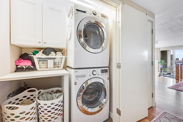 washroom featuring cabinet space, stacked washer and dryer, and wood finished floors
