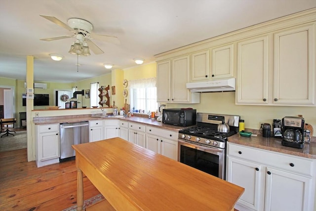 kitchen with under cabinet range hood, a peninsula, appliances with stainless steel finishes, and cream cabinetry