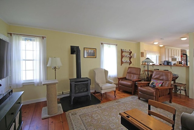 living room with crown molding, baseboards, a wood stove, and wood-type flooring